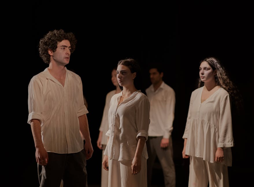 A group of performers in white attire engaged in a theater production on stage